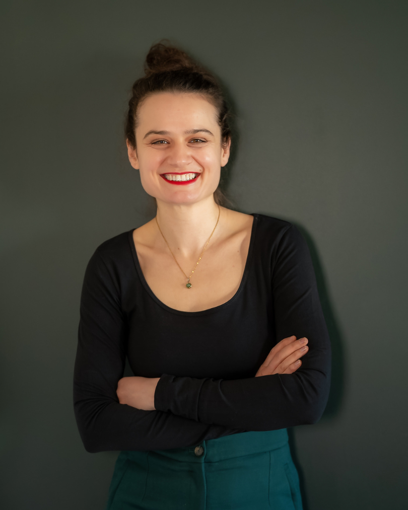 Katharina Dellos – Moderatorin, Mediatorin und Trainerin für Kommunikation und Konfliktmanagement, lächelnd vor dunkelgrünem Hintergrund